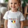 Fetiță zâmbitoare poartă tricou personalizat patriotic Româncuța cu inimă tricoloră și nume imprimat, în casă luminoasă